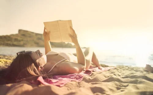 Vrouw licht op het strand en leest een boek in bikini